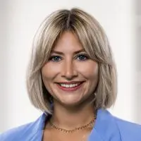 Porträt einer Frau mit blonden Haaren und blauer Jacke, die in die Kamera lächelt.