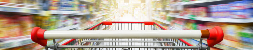 Ein Einkaufswagen mit rotem Griff in einem Supermarkt mit verschwommenen Regalen im Hintergrund.
