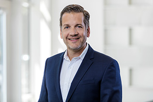 Porträt von Marc Kloepfel in einem Anzug mit einem neutralen Hintergrund.