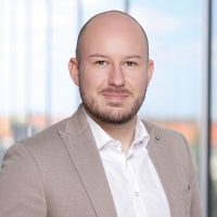 Porträt eines Mannes mit Glatze in einem hellen Anzug und weißem Hemd.