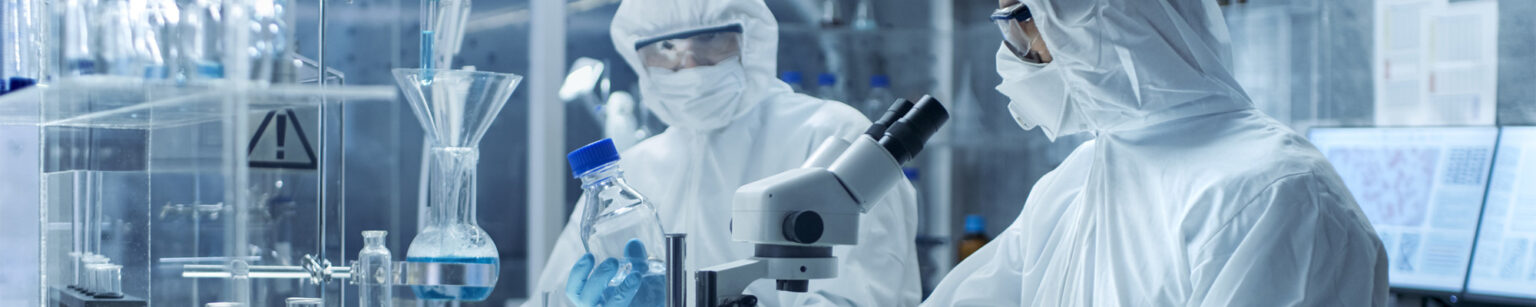Wissenschaftler in Schutzkleidung, die ein Mikroskop in einem Labor verwenden.