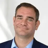 Porträt eines Mannes mit kurzem Haar, der einen blauen Anzug und ein hellblaues Hemd trägt.