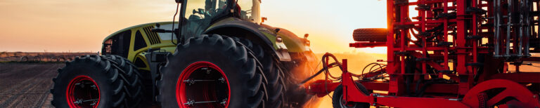 Ein Traktor mit großen Reifen zieht landwirtschaftliches Gerät bei Sonnenuntergang über ein Feld.