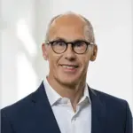 Porträt eines Mannes mit Brille, der in einem Anzug und Hemd gekleidet ist.