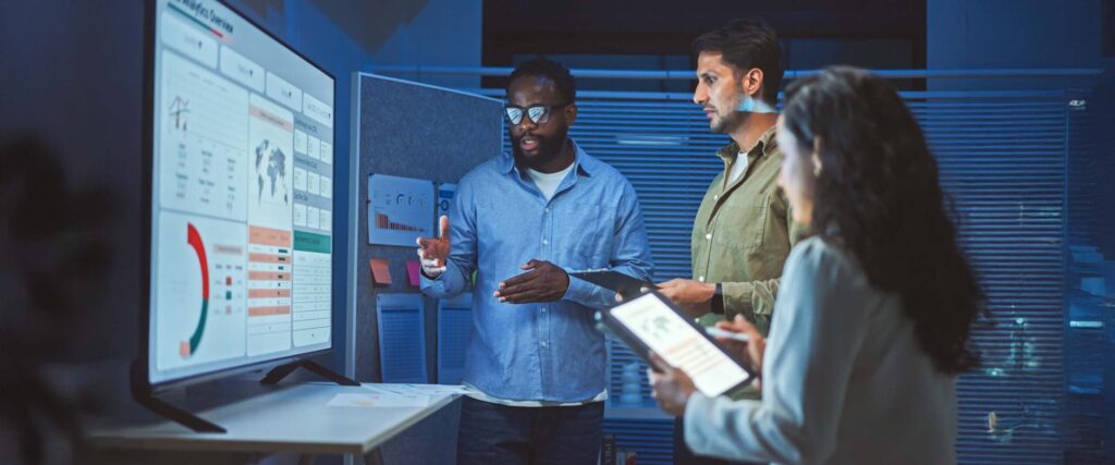 Three people in a meeting discussing a presentation on a screen.