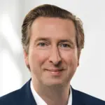 Porträt eines Mannes mit kurzen, hellen Haaren, der einen blauen Anzug trägt.