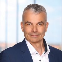 Porträt eines Mannes mit grauen Haaren, der einen blauen Anzug und ein weißes Hemd trägt.