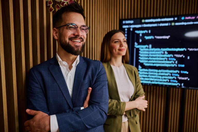 Ein Mann in einem blauen Anzug und eine Frau in einem grünen Blazer stehen in einem modernen Büro.
