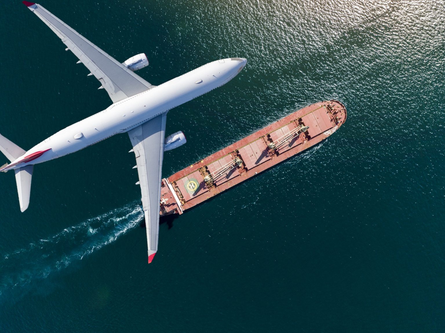 Ein Flugzeug fliegt über ein Frachtschiff auf dem Wasser.