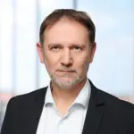 Porträt eines Mannes mit Bart, der einen schwarzen Anzug und ein weißes Hemd trägt.