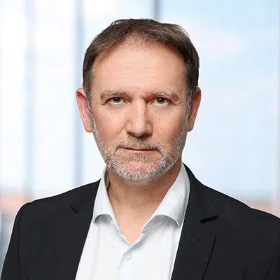 Porträt eines Mannes mit Bart, der einen schwarzen Anzug und ein weißes Hemd trägt.