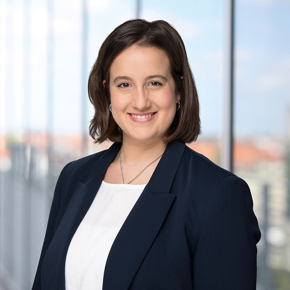 Portrait einer Frau mit braunen Haaren, die einen dunkelblauen Anzug trägt und lächelt.