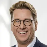 Porträt eines Mannes mit Brille und blondem Haar, der lächelt.