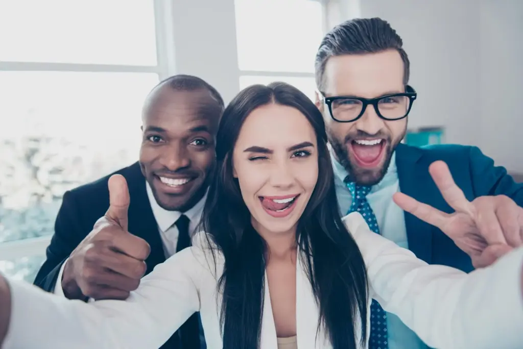 Drei Personen in formeller Kleidung posieren für ein Selfie in einem Büro.