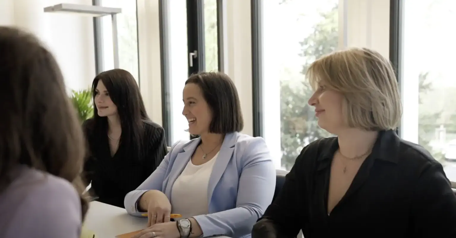Drei Frauen sitzen an einem Tisch in einem Besprechungsraum und unterhalten sich.