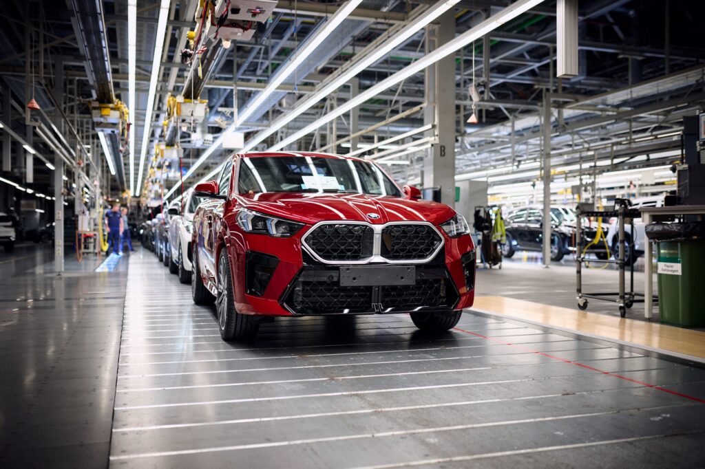 Roter BMW X5 steht in einer Produktionshalle mit weiteren Fahrzeugen im Hintergrund.