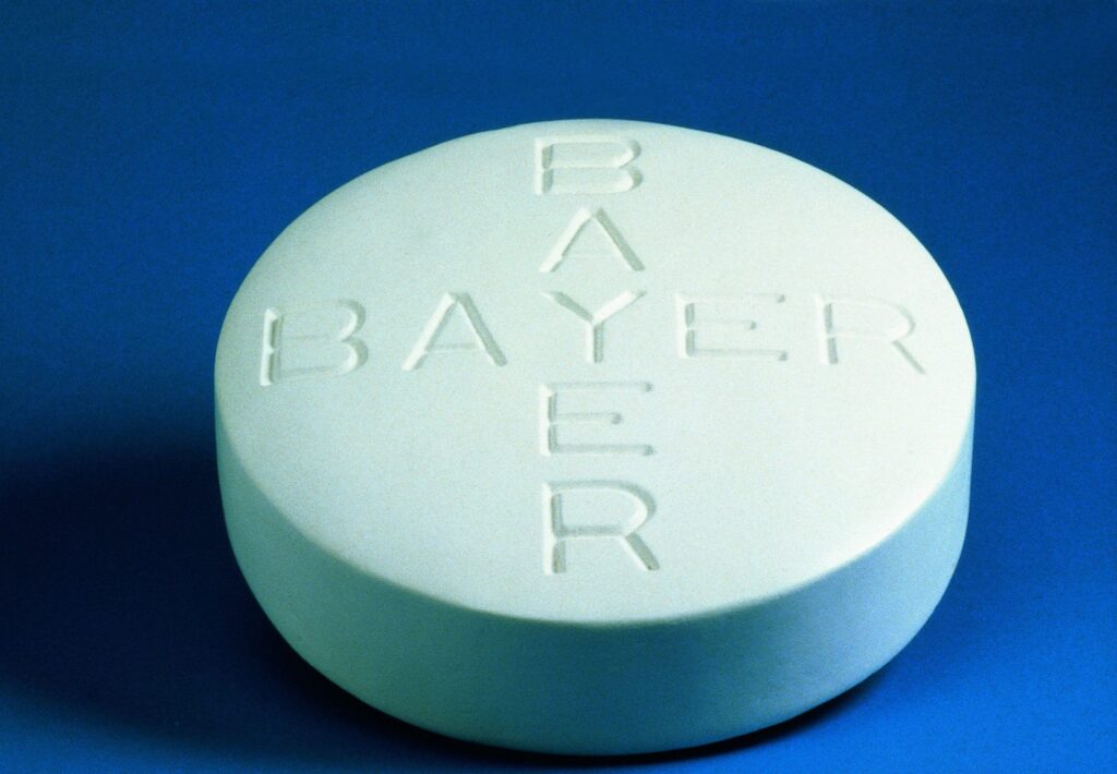 Runde Bayer Aspirin Tablette mit eingraviertem Schriftzug auf blauer Oberfläche.