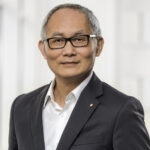 Porträt von Shinya Yamanaka in einem Anzug mit Brille vor einem neutralen Hintergrund.