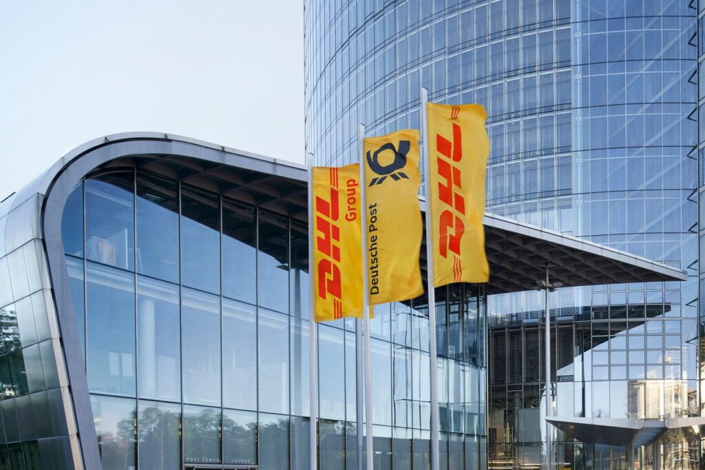 Drei Flaggen der DHL Group und Deutsche Post vor einem modernen Gebäude.