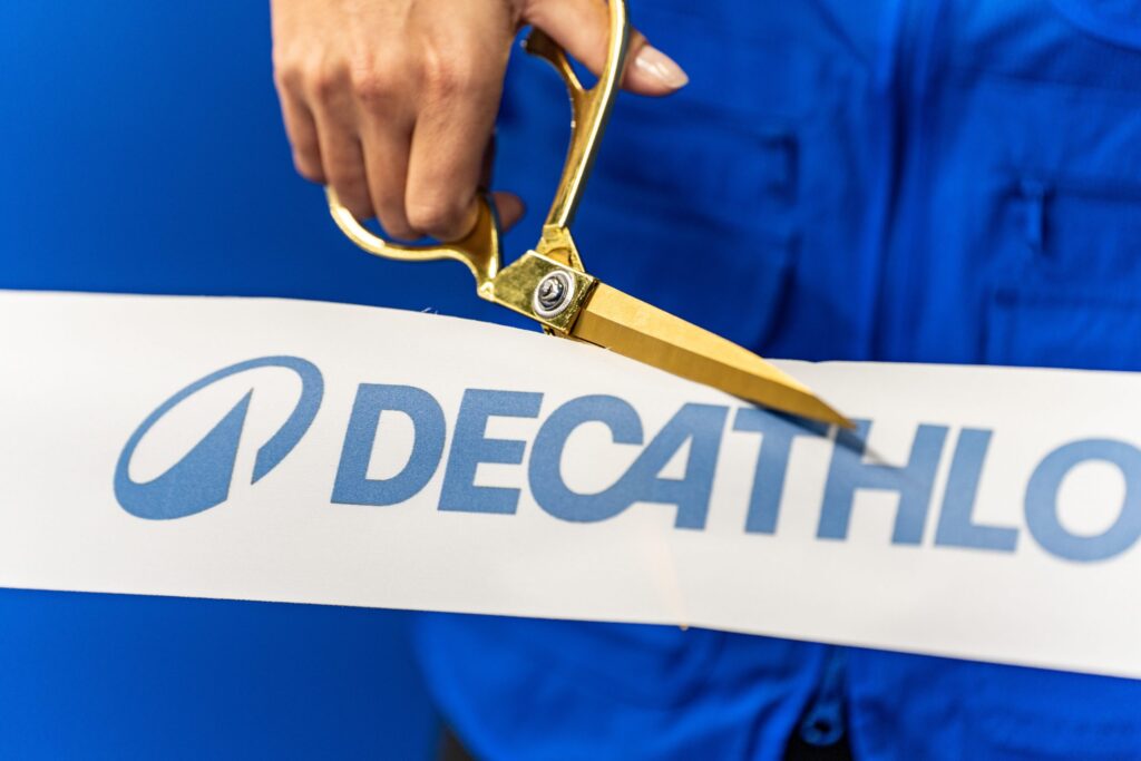 Eine Hand hält eine goldene Schere, die ein Band mit dem Decathlon-Logo schneidet.