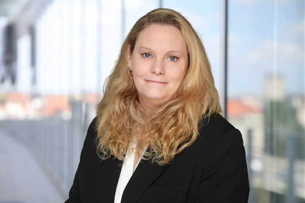 Porträt von Denise Roggenbruck in einem schwarzen Blazer mit langen, lockigen Haaren.