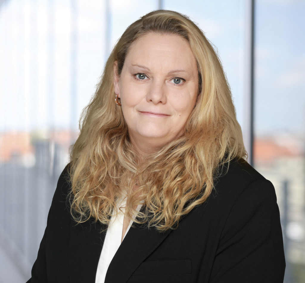 Porträt von Denise Roggenbuck mit langen, lockigen Haaren und einem schwarzen Blazer.