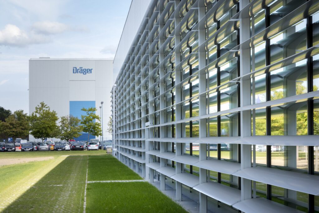 Fassade des Dräger Produktionsstandorts in Lübeck mit modernen Fenstern und angrenzendem Parkplatz.