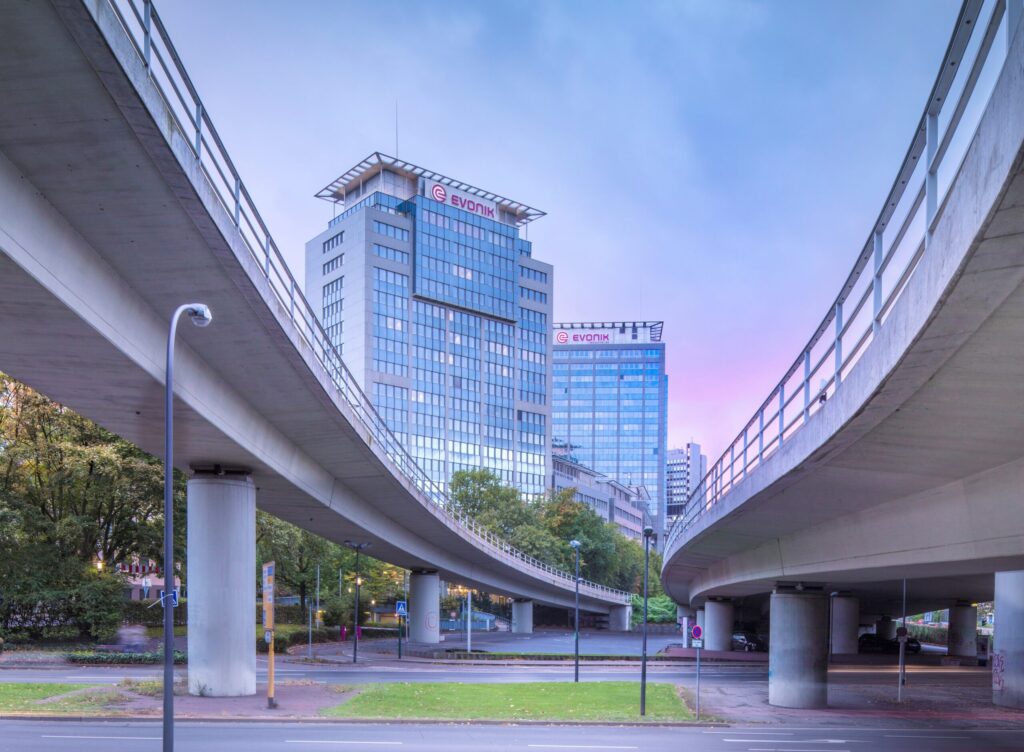 Moderne Gebäude von Evonik mit Überführung im Vordergrund und einem klaren Himmel im Hintergrund.