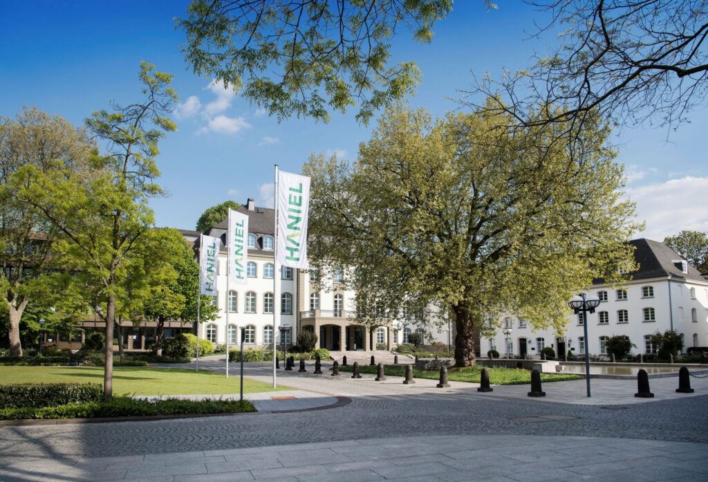 Das Haniel Gebäude mit Fahnen und Bäumen im Vordergrund, umgeben von einem gepflasterten Weg.