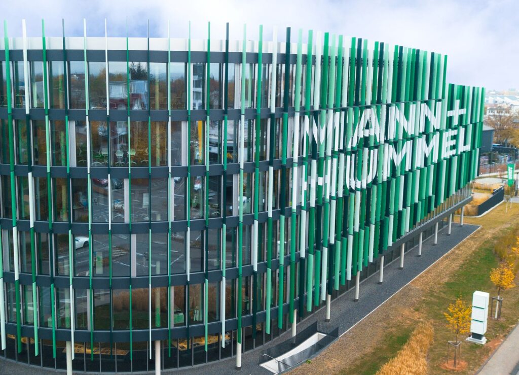 Moderne Architektur des Mann + Hummel Gebäudes mit grünen und transparenten Elementen.