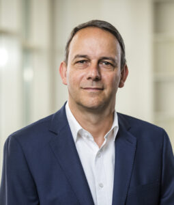 Portrait eines Mannes in einem Anzug mit einem neutralen Gesichtsausdruck.