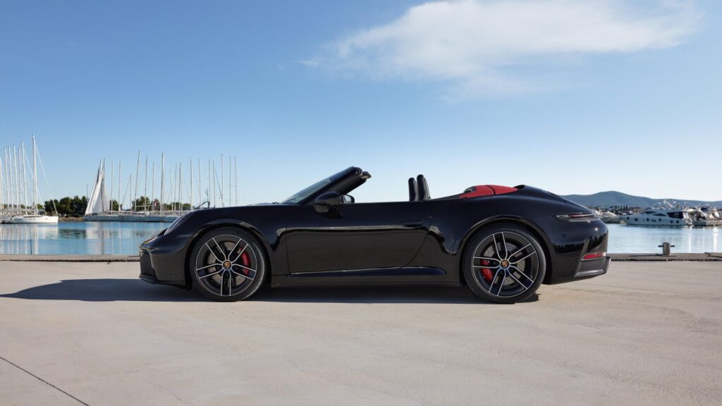 Schwarzer Porsche 911 Carrera GTS Cabriolet 2024 mit rotem Innenraum auf einem Parkplatz.