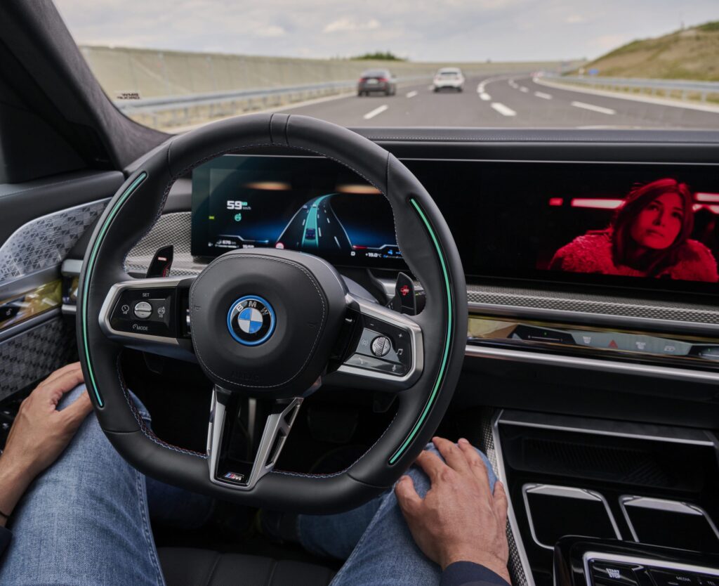 Cockpit eines BMW mit autonomem Fahrdisplay und Fahrerin auf dem Bildschirm.