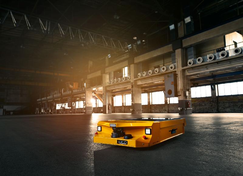 Gelbes automatisiertes Transportsystem in einer großen Industriehalle mit Fenstern.