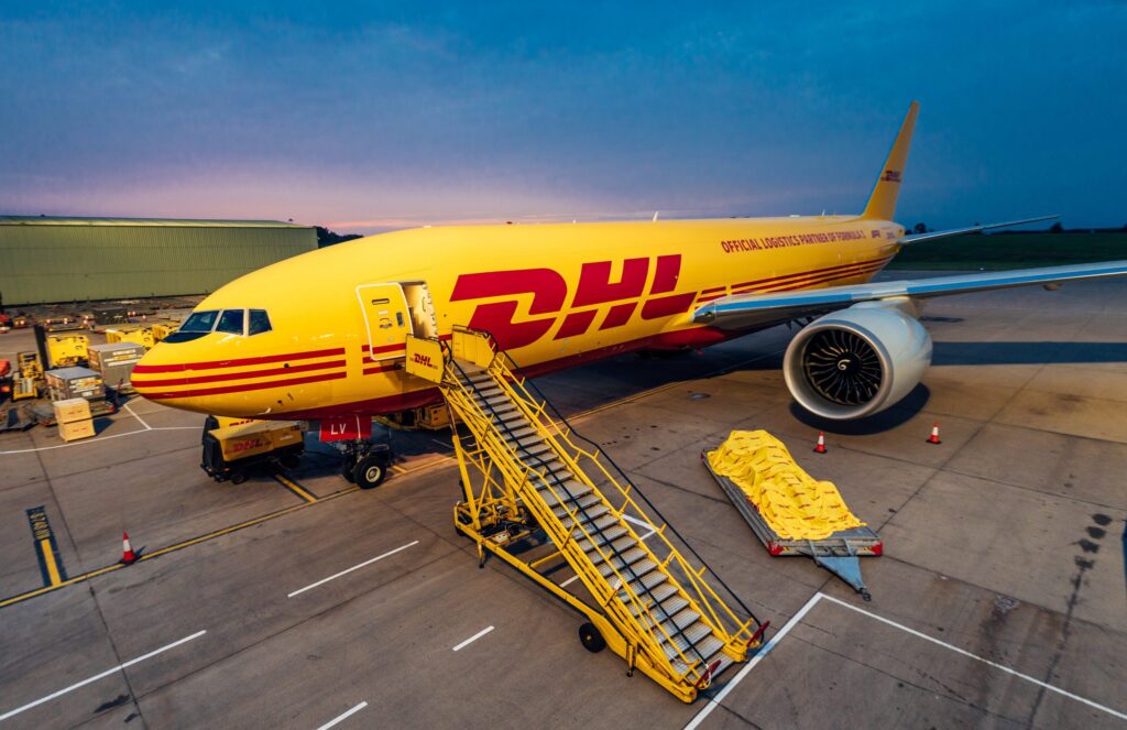 Ein DHL-Flugzeug steht am Flughafen mit einer Treppe und Fracht auf dem Boden.
