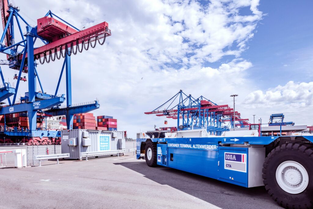 Transportfahrzeug im Containerterminal mit Krananlagen im Hintergrund.