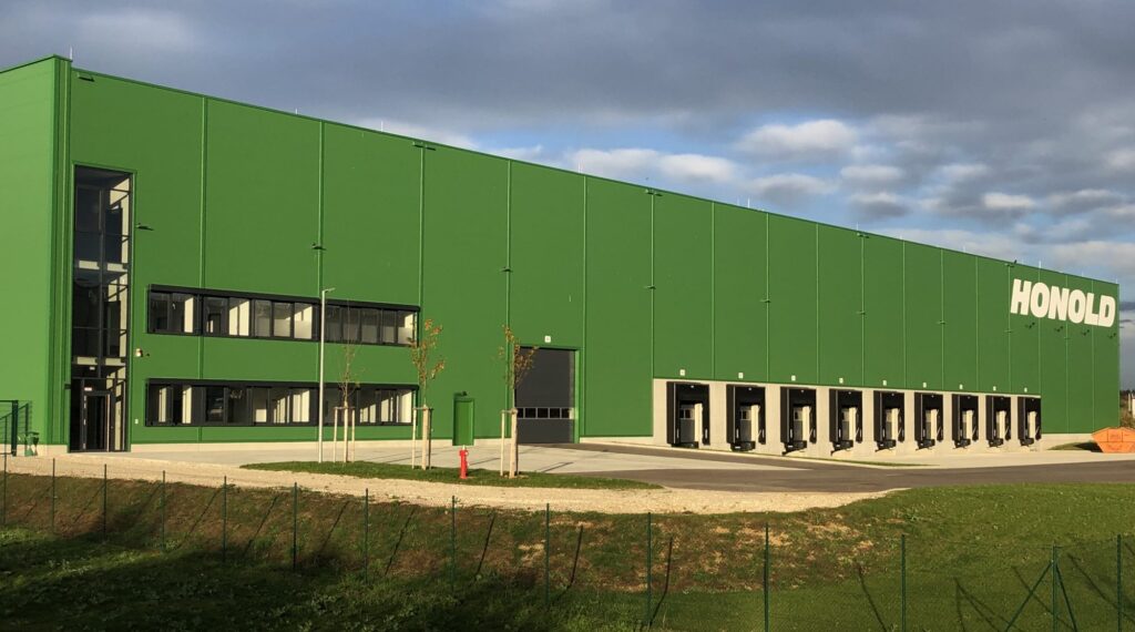 Grünes Lagergebäude mit dem Schriftzug 'HONOLD' an der Fassade und mehreren Laderampen.
