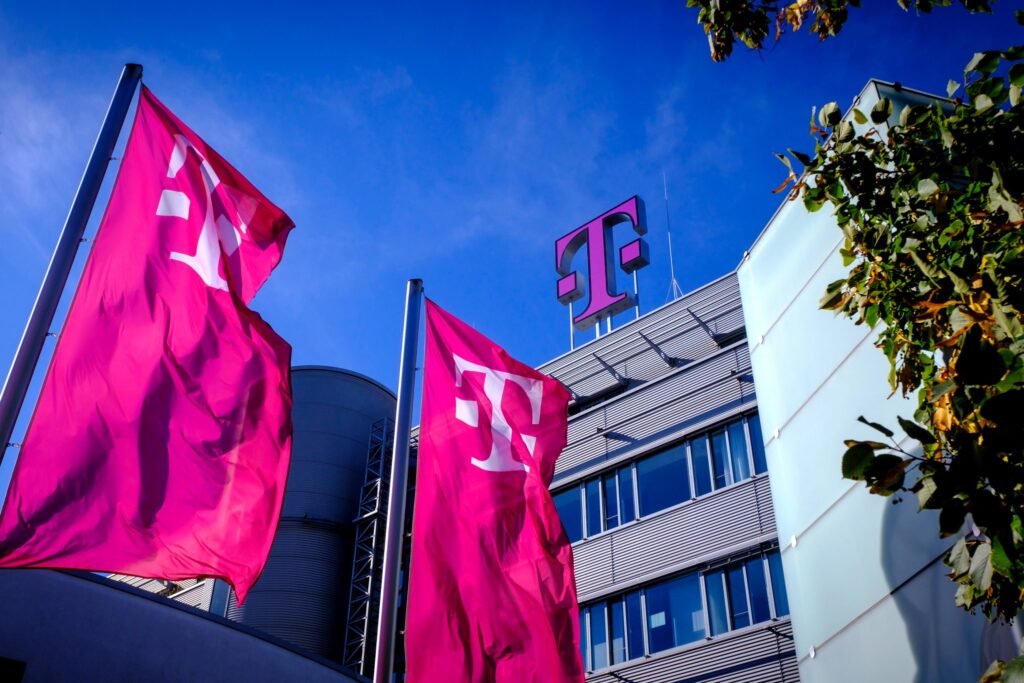 Fahnen mit dem Telekom-Logo vor einem modernen Gebäude mit blauer Himmel im Hintergrund.