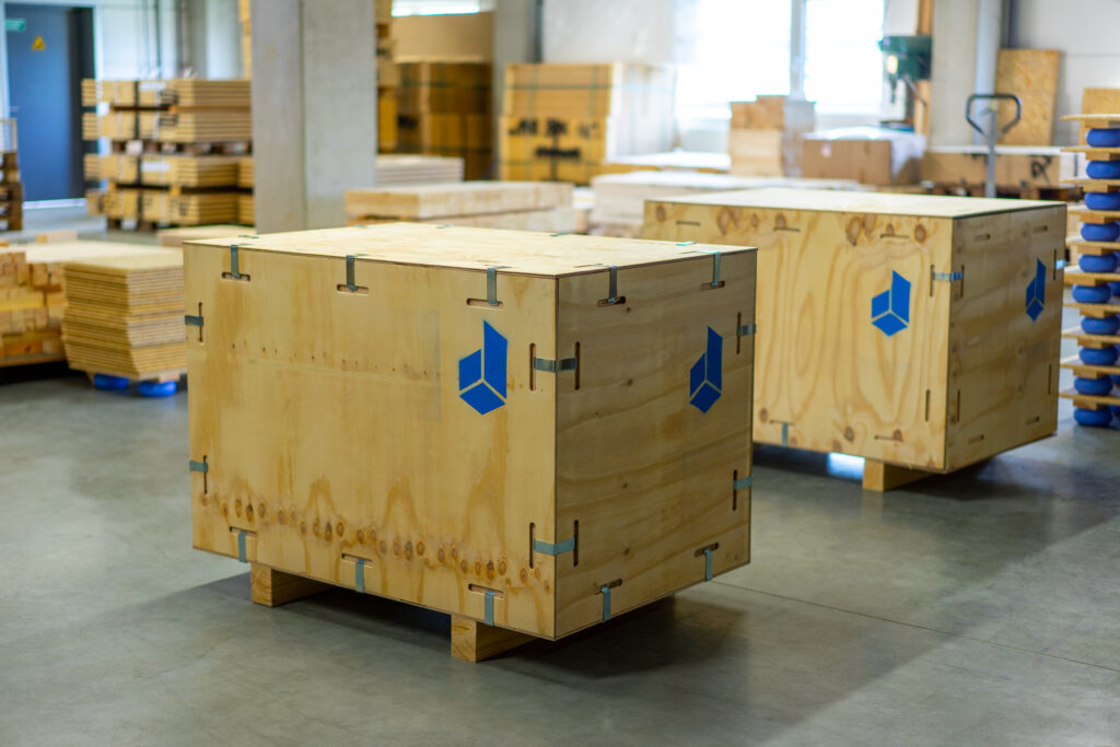 Zwei Holzverpackungskisten mit blauen Logos in einer Lagerumgebung.