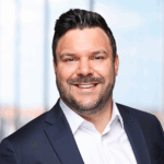 Porträt von Sascha Kramer in einem Anzug mit einem Lächeln vor einem hellen Hintergrund.