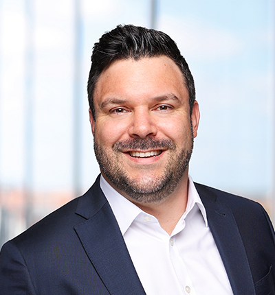 Porträt von Sascha Kramer in einem Anzug mit einem Lächeln vor einem hellen Hintergrund.