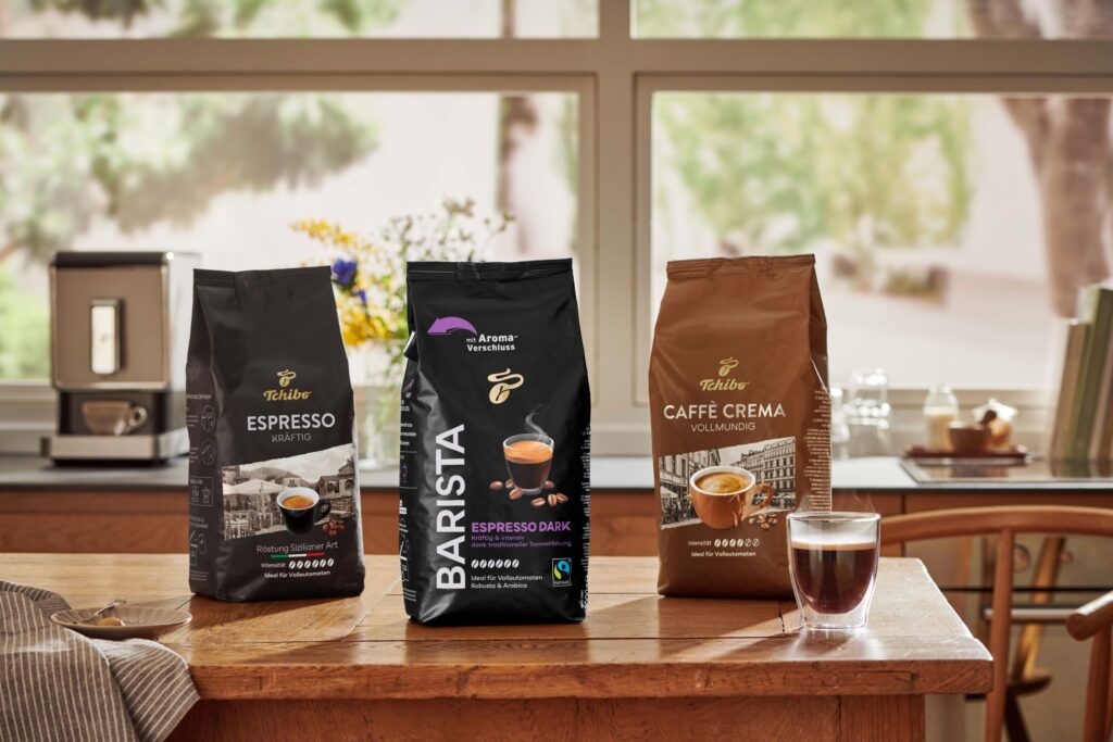 Drei verschiedene Kaffeeverpackungen von Tchibo auf einem Tisch, darunter Espresso, Barista und Caffè Crema.