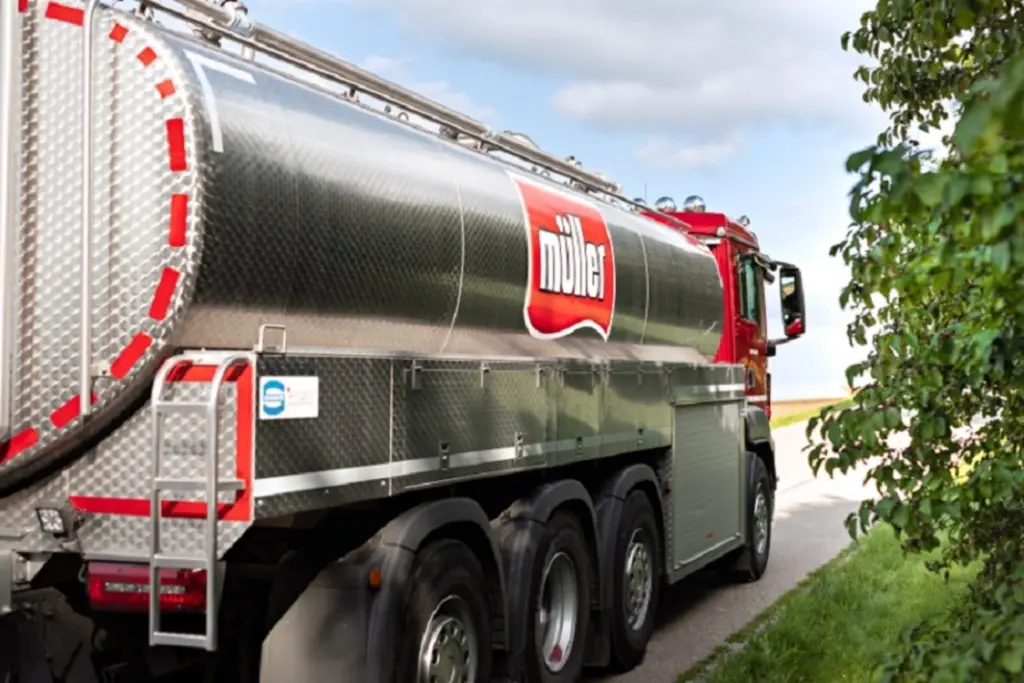 Silberner Milchsammelwagen mit rotem Müller-Logo auf der Seite, geparkt an einer Straße.