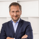 Portrait of a man in a suit with folded arms and a smiling face.