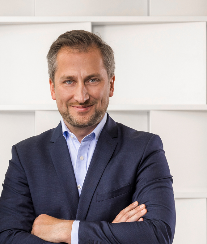 Portrait of a man in a suit with folded arms and a smiling face.