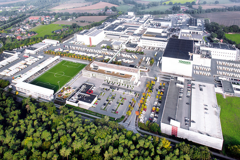Luftaufnahme eines großen Industriekomplexes mit einem Fußballfeld und Lkw-Ladebereichen.