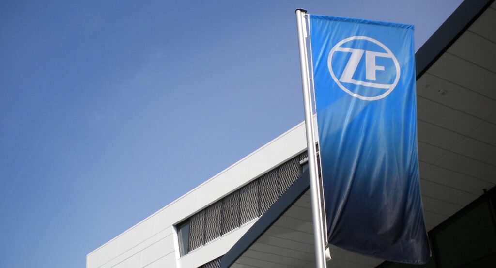Flagge mit dem ZF-Logo weht vor einem modernen Gebäude unter blauem Himmel.