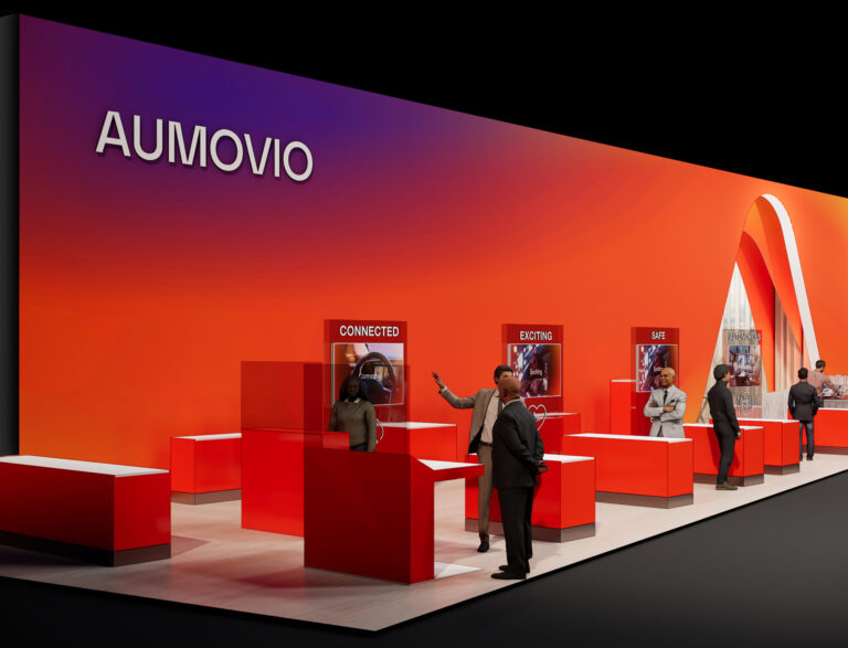 AUMOVIO Messestand mit roten Ausstellungsflächen und Personen, die sich unterhalten.