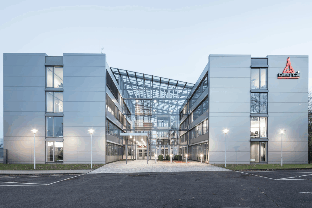 Moderne Bürogebäude der Deutz AG mit Glasdach und beleuchteten Eingangsbereich.