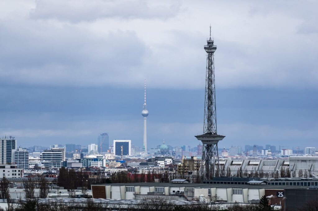 Berlin Funkturm im Vordergrund mit dem Fernsehturm im Hintergrund unter bewölktem Himmel.